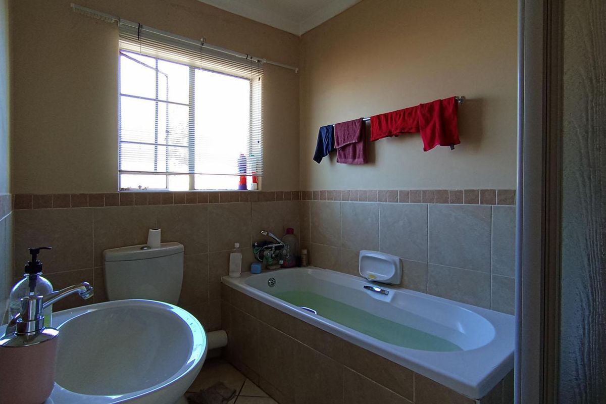 A functional bathroom featuring a built-in bathtub, pedestal basin, and toilet, finished with neutral ceramic wall and floor tiles.