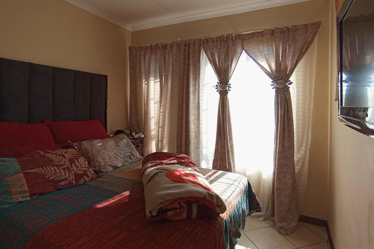 A bedroom featuring tiled flooring and cove cornicing, with natural light entering through a window dressed with curtains.