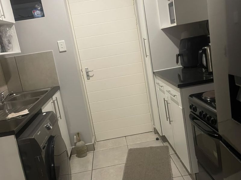 A functional kitchen featuring white cabinetry, granite countertops, tiled flooring, and space for a washing machine, leading to an exterior door.
