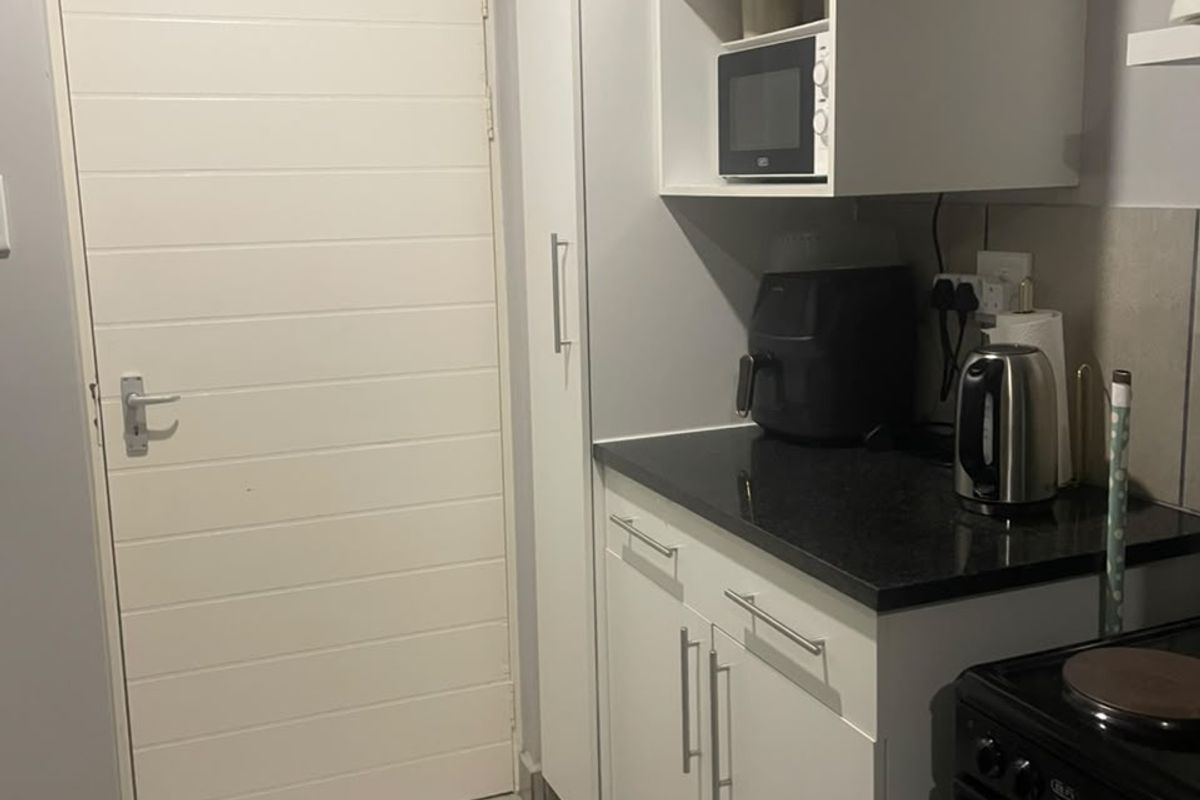 A compact kitchen area featuring white cabinetry, dark stone countertops, a built-in microwave, and tiled flooring, providing a functional and clean workspace.