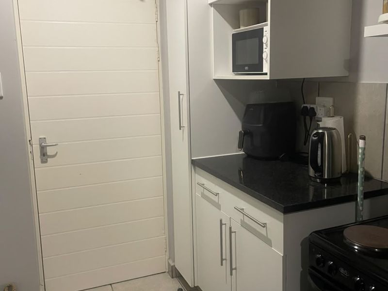 A compact kitchen area featuring white cabinetry, dark stone countertops, a built-in microwave, and tiled flooring, providing a functional and clean workspace.