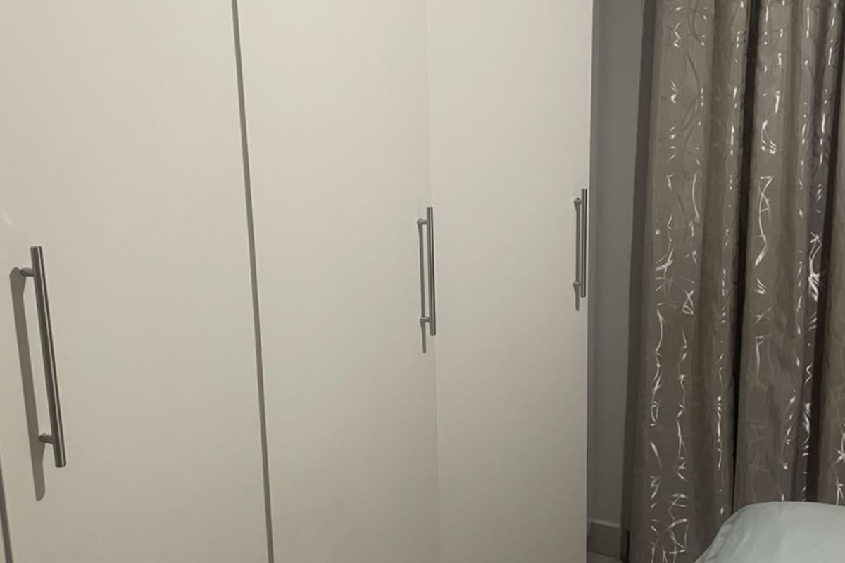 A bedroom featuring a white built-in wardrobe with modern metal handles and tiled flooring.