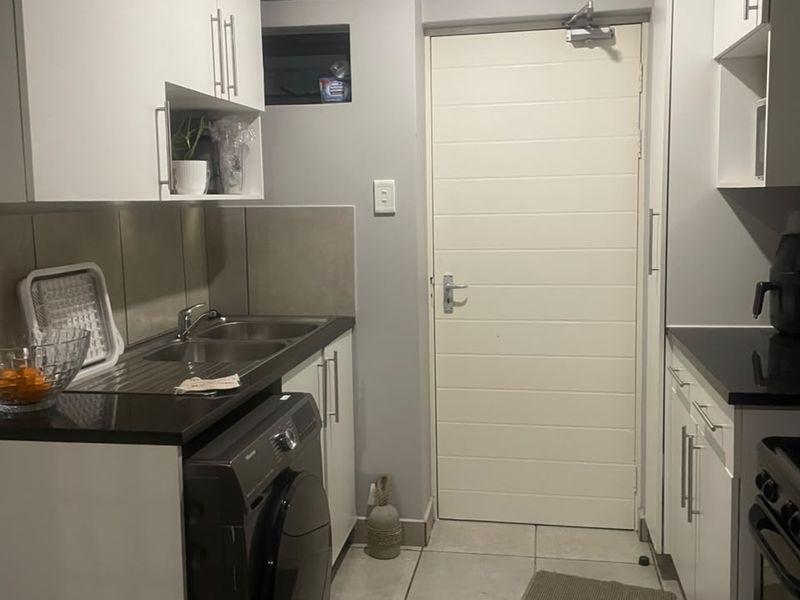 A functional kitchen featuring white cabinetry, black granite countertops, a double bowl stainless steel sink, and tiled flooring with direct access to an exterior door.
