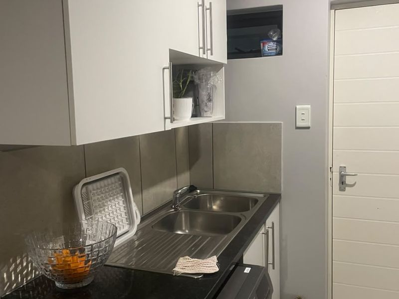 A compact kitchen area featuring modern white cabinetry, a double sink with stone countertops, and tiled backsplash finishes.