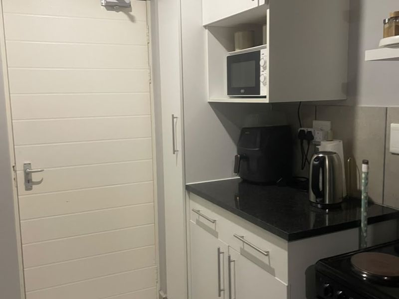 A compact kitchen area featuring white built-in cabinetry, dark granite countertops, a built-in microwave, and tiled flooring with a secure door.
