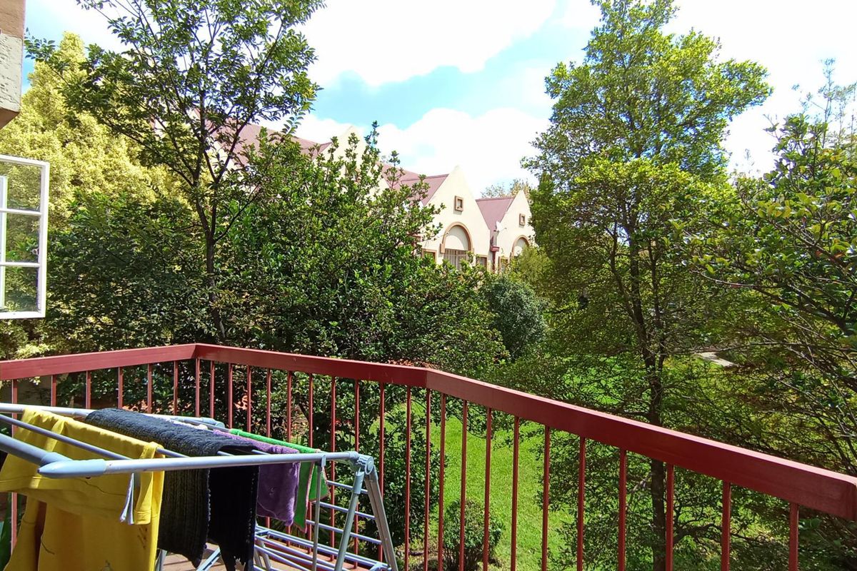 A private balcony featuring a metal balustrade and views over the surrounding garden and neighboring apartment complex.