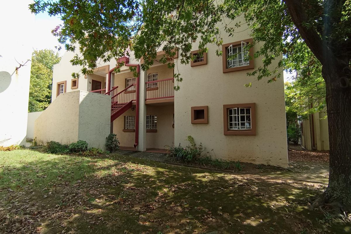 Exterior view of a multi-story apartment building featuring a stucco facade, metal staircase, and security-barred windows set within a landscaped garden area.