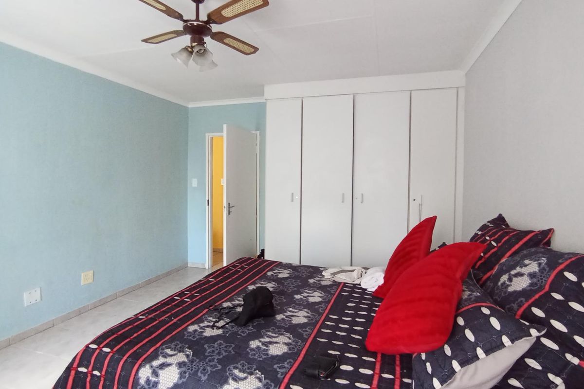A bedroom featuring built-in cupboards, a ceiling fan, and tiled flooring, providing a functional space with neutral wall finishes.