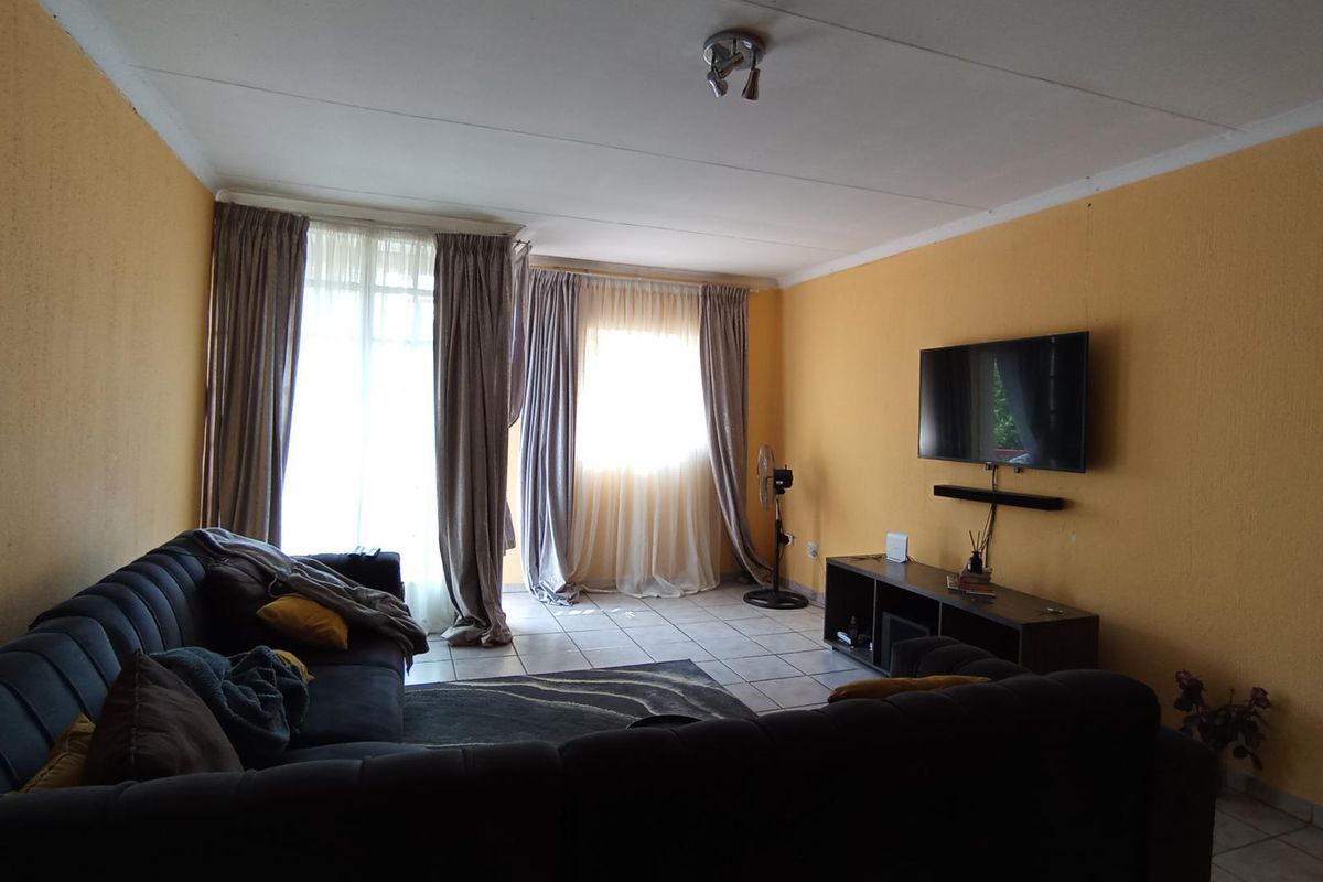 A living room featuring tiled flooring and natural light through large windows with curtains.