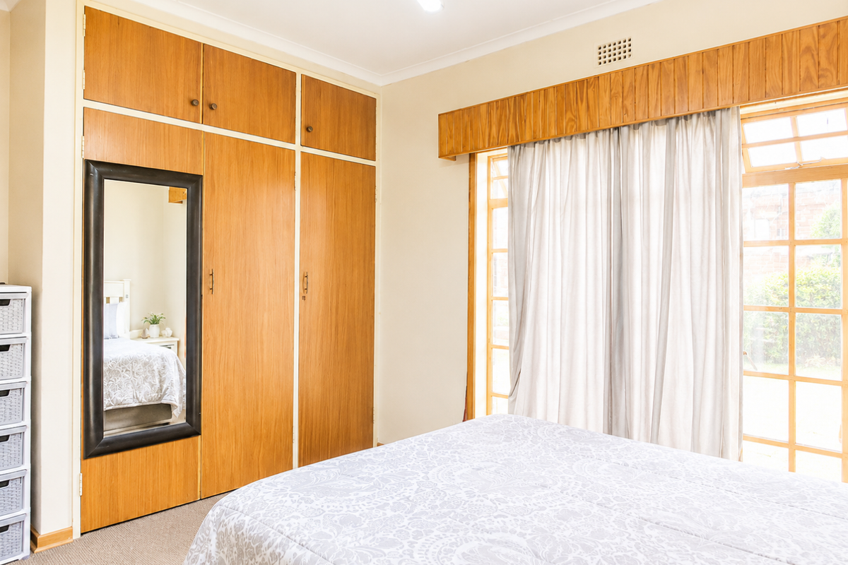 A bedroom featuring built-in wooden cabinetry, carpeted flooring, and large timber-framed windows providing natural light and garden access.