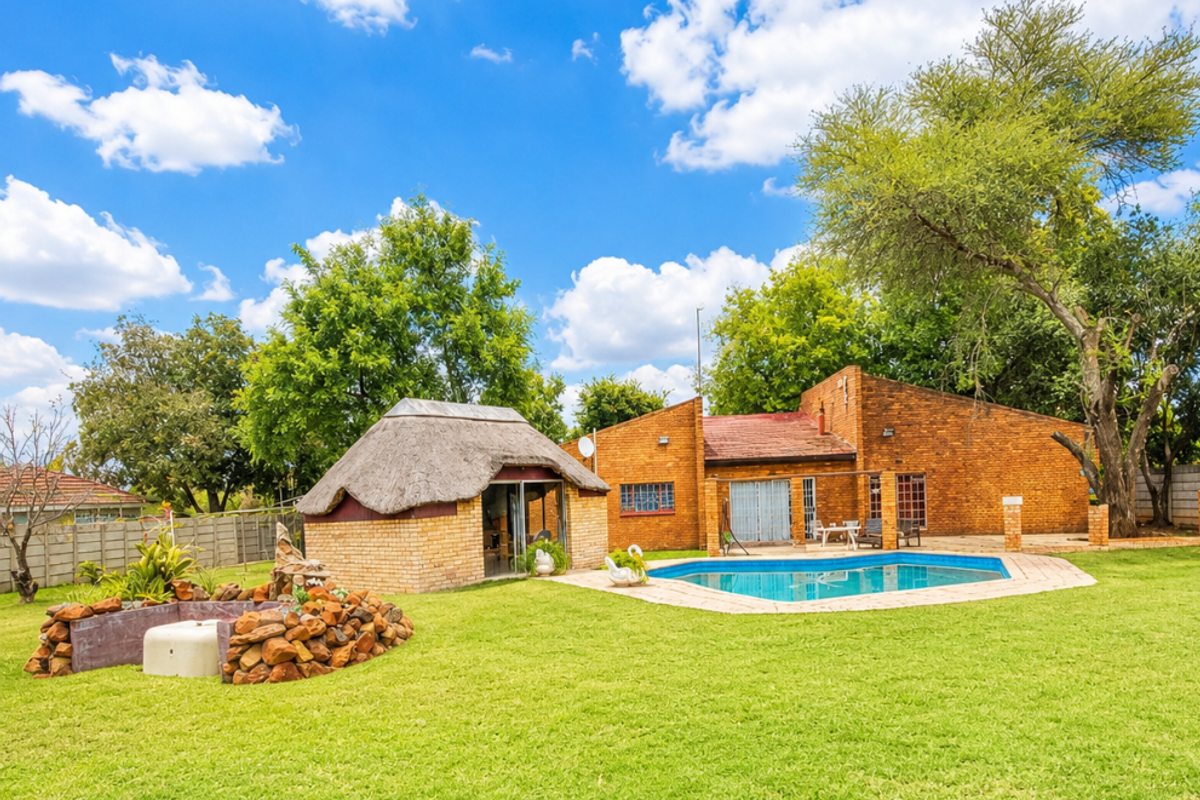 Spacious rear garden featuring a swimming pool, paved surround, and a traditional thatched lapa, set against a brick-built residential home.