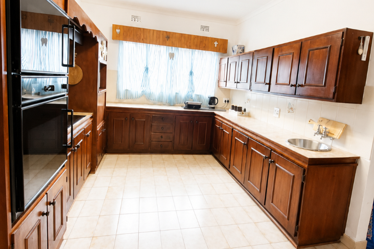 A spacious kitchen featuring extensive wooden cabinetry, a double wall oven, tiled flooring, and a functional layout with ample counter space.