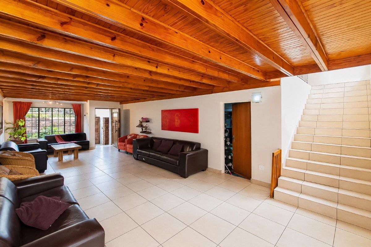 Spacious living area featuring exposed timber beam ceilings, neutral tiled flooring, and a tiled staircase leading to the upper level.