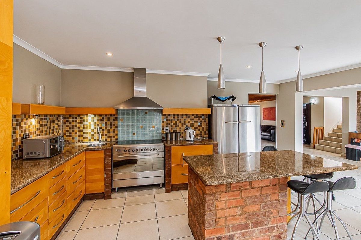 A functional kitchen featuring granite countertops, a stainless steel stove with extractor, mosaic backsplash, and a unique exposed brick island with breakfast seating.