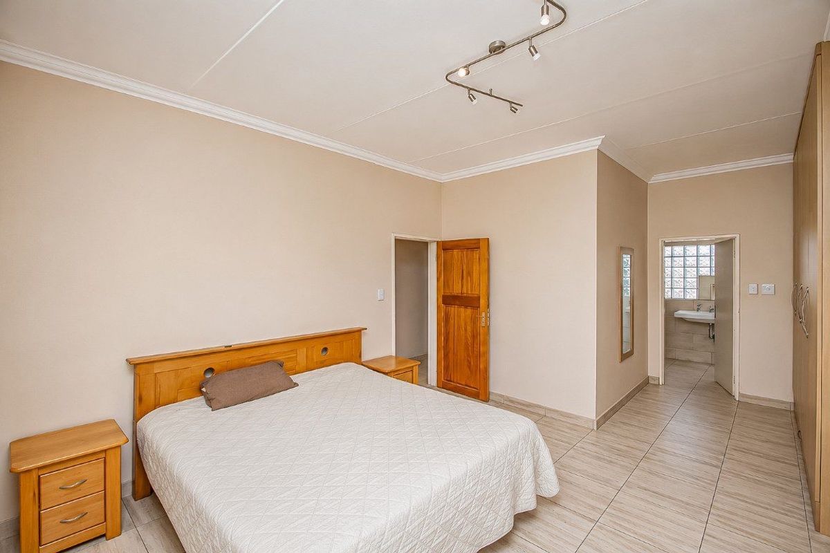 Spacious bedroom featuring tiled flooring, built-in cupboards, and direct access to an en-suite bathroom with modern track lighting.