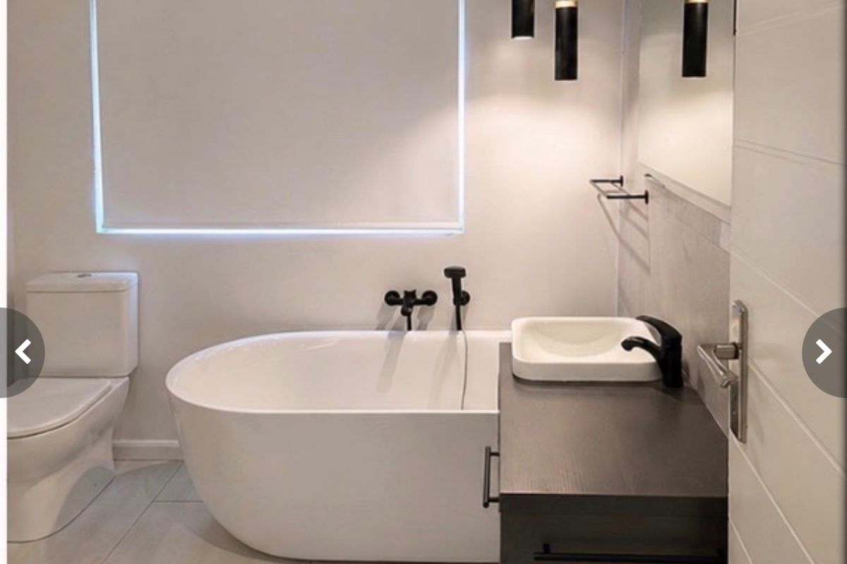 Modern bathroom featuring a sleek freestanding bathtub, dark vanity with vessel sink, matte black fixtures, and contemporary pendant lighting.