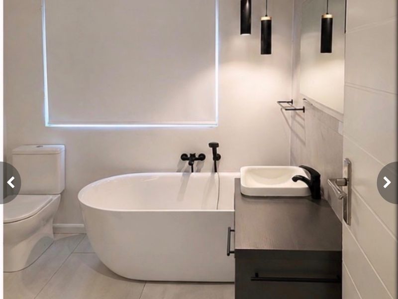 Modern bathroom featuring a sleek freestanding bathtub, dark vanity with vessel sink, matte black fixtures, and contemporary pendant lighting.