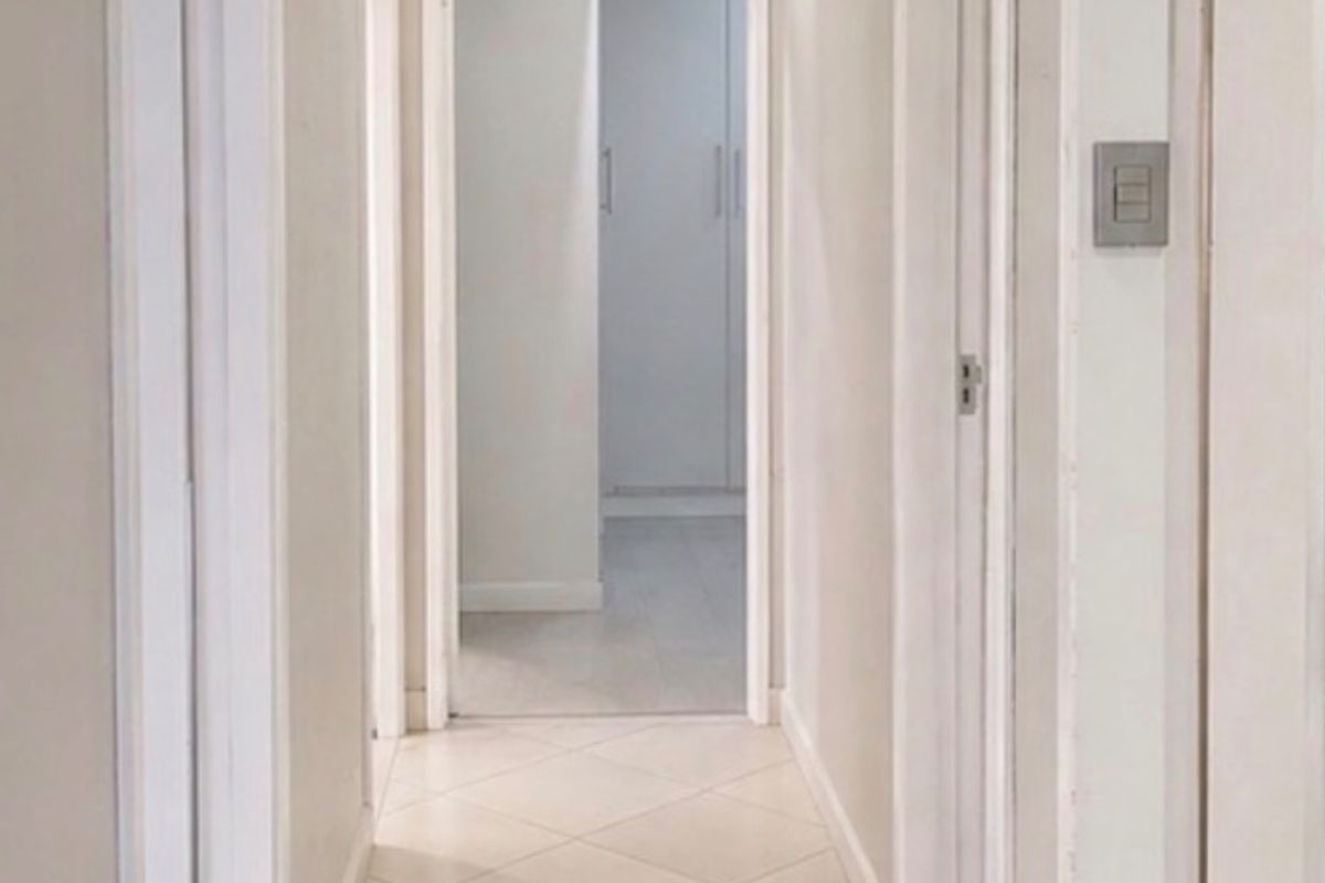 A clean, well-lit hallway featuring neutral tiled flooring and white door frames, providing access to multiple rooms.
