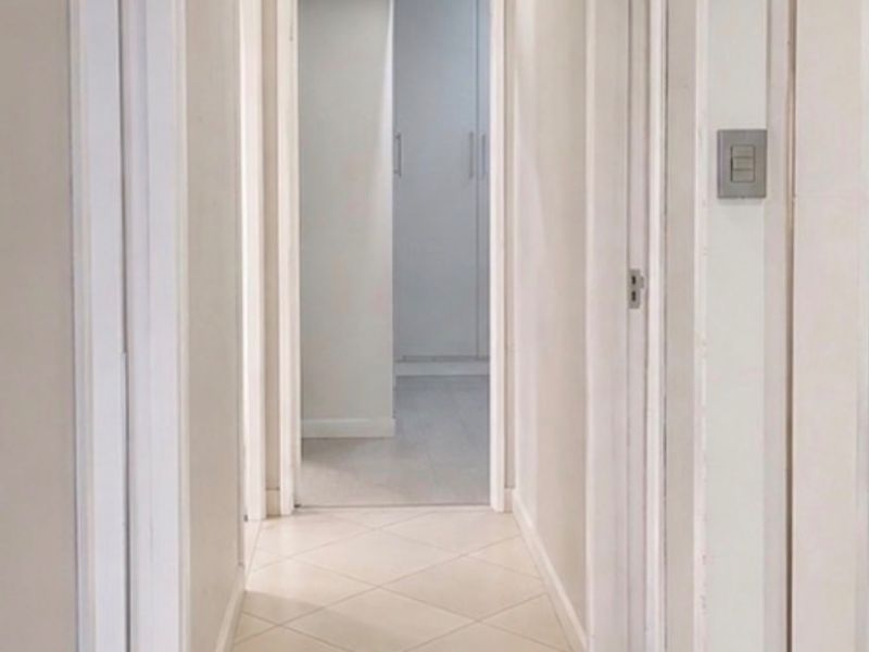 A clean, well-lit hallway featuring neutral tiled flooring and white door frames, providing access to multiple rooms.