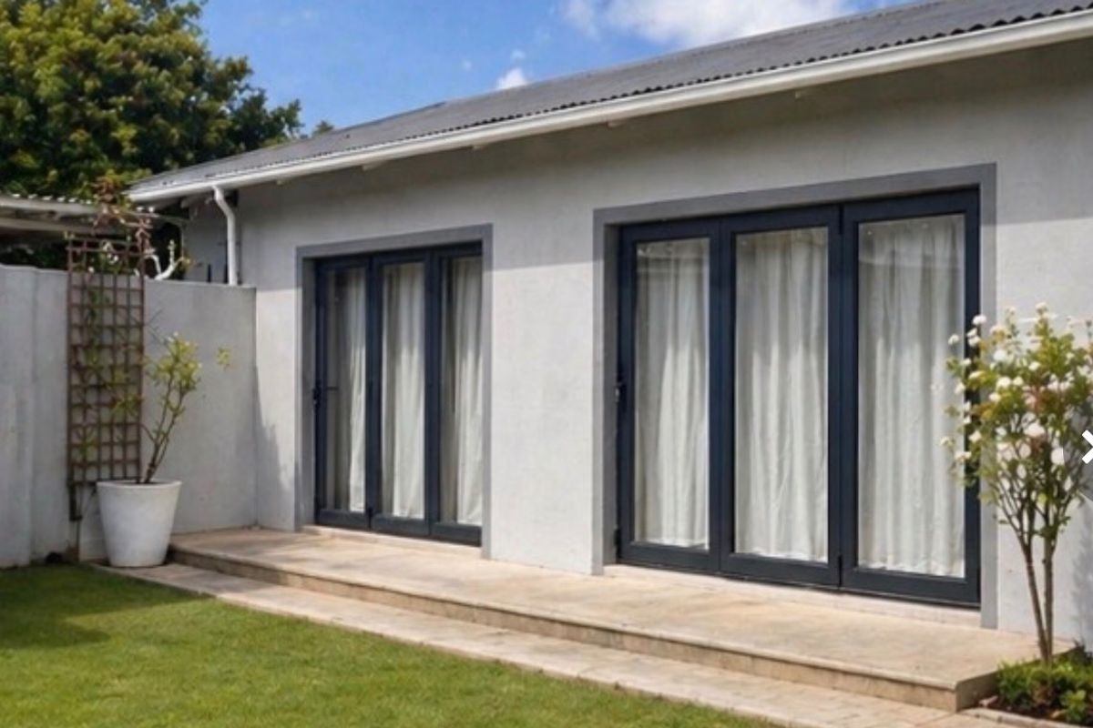 Rear exterior view featuring a paved patio area with modern dark-framed bi-fold doors leading into the home, set against a well-maintained garden.