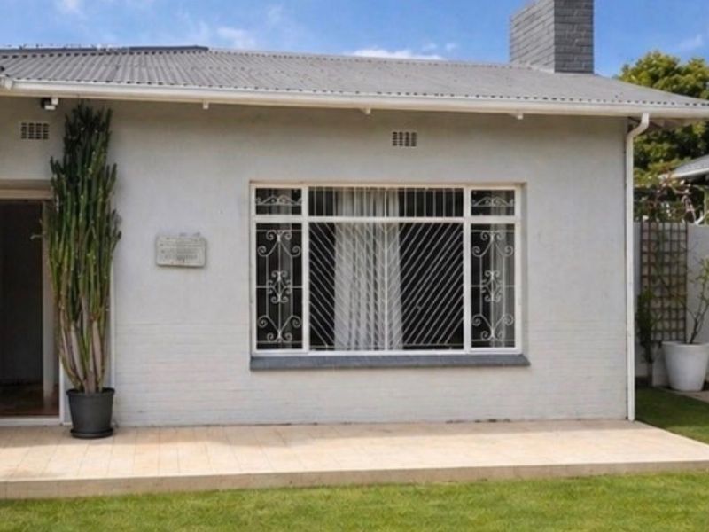 Front facade of the house featuring a tiled patio, corrugated metal roof, brick chimney, and security-barred windows.
