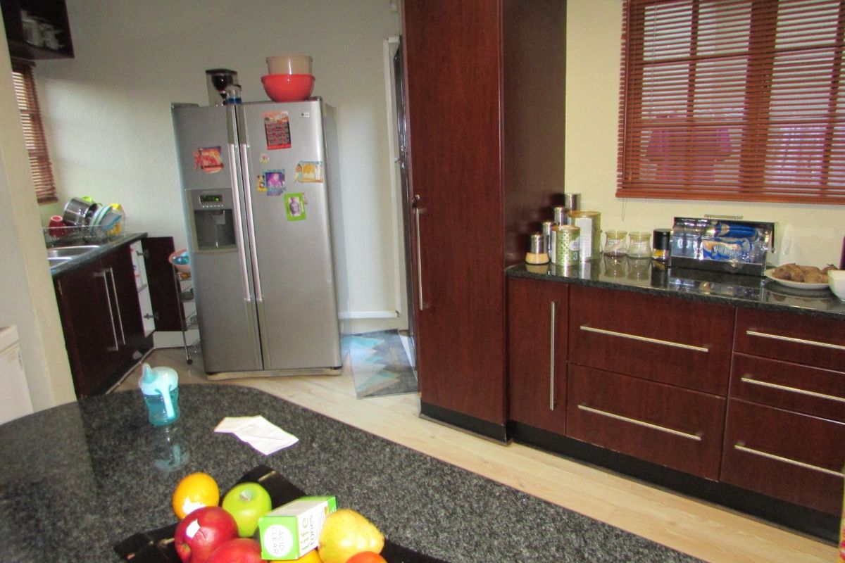 A functional kitchen featuring dark wood cabinetry, granite countertops, and a double sink, with natural light provided by windows with venetian blinds.