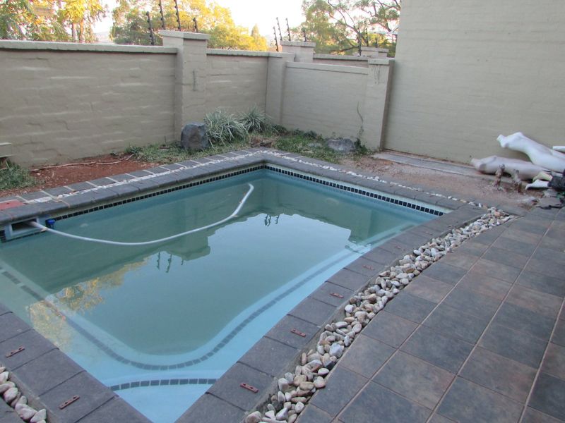 A small swimming pool area featuring a tiled surround, perimeter wall with electric fencing, and an adjacent unmaintained garden space.