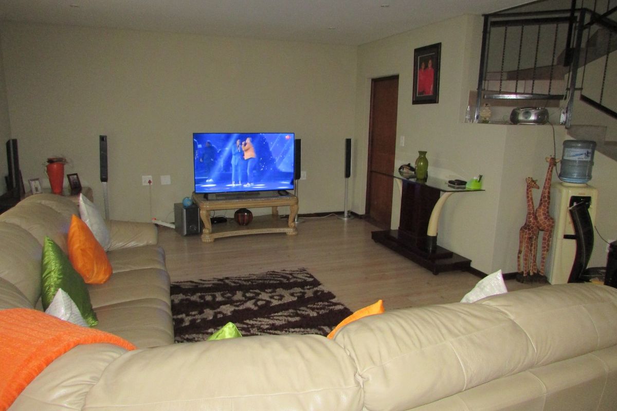 A living room area featuring laminate flooring, recessed lighting, and an open staircase with a metal railing.