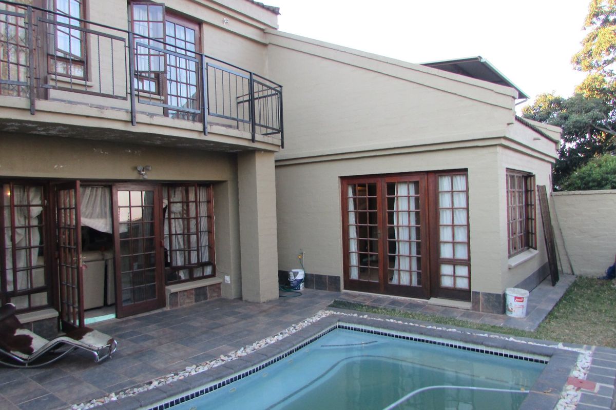 Rear exterior view of the townhouse featuring a swimming pool, tiled patio area, upper-level balcony, and timber-framed glass doors leading into the home.