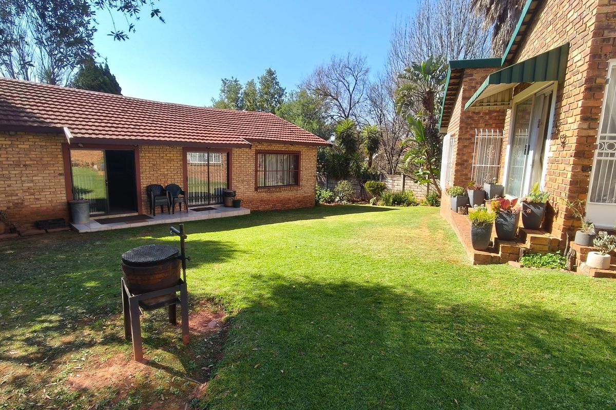 A spacious rear garden area featuring a well-maintained lawn, face brick exterior walls, and access to the home via sliding doors.