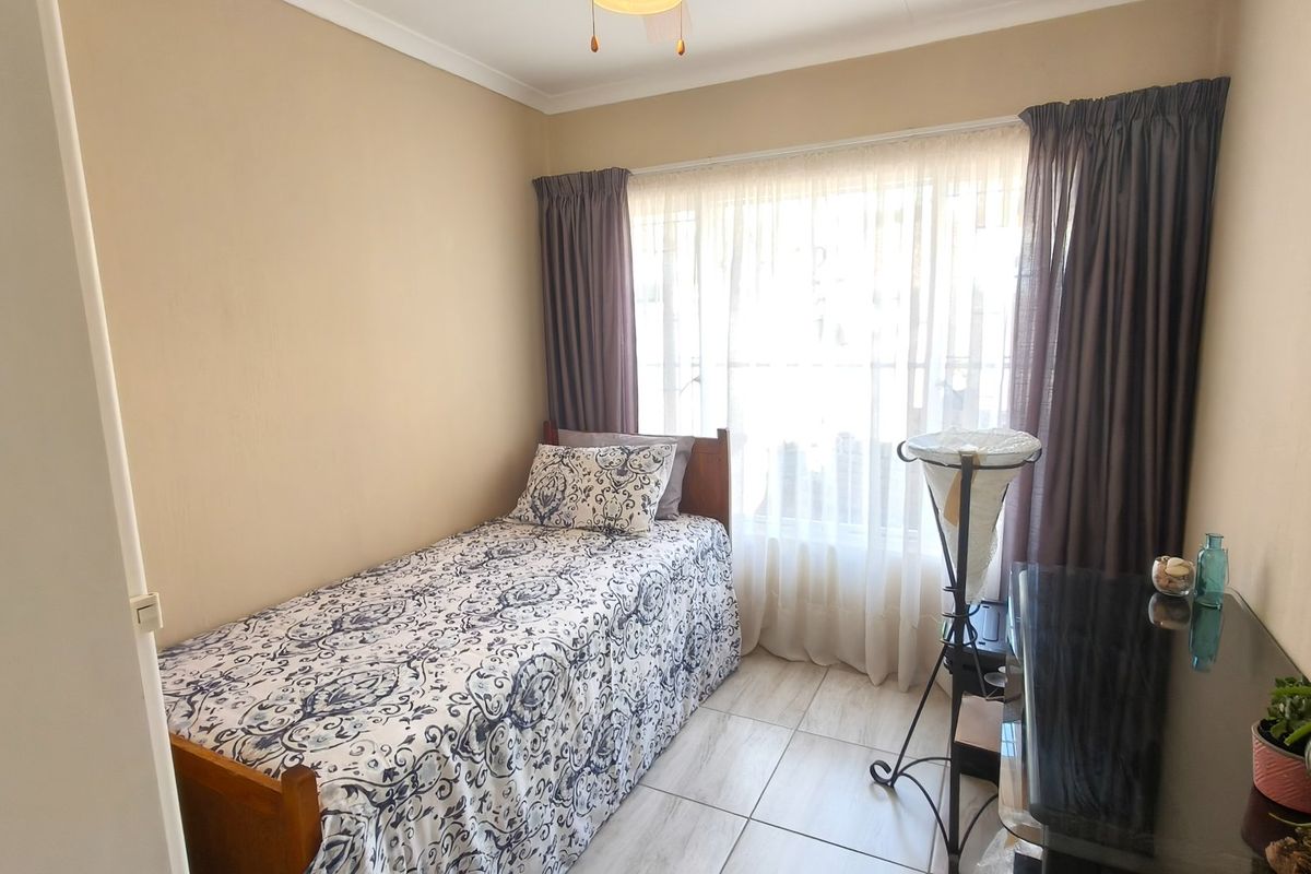 A compact bedroom featuring tiled flooring and a ceiling fan, with large windows allowing for natural light.