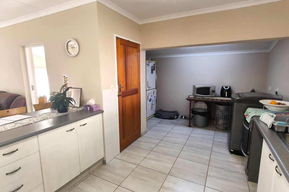 A functional kitchen area featuring tiled flooring, built-in cabinetry with laminate countertops, and a timber door leading to an adjacent utility space.