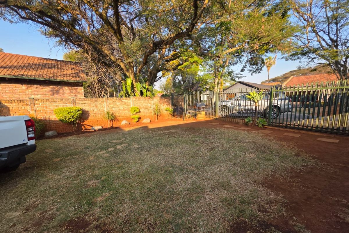 A private rear garden area featuring a lawn, brick boundary wall, and metal security gate access.