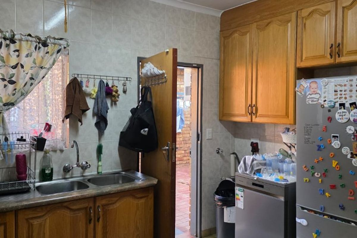 A functional kitchen featuring traditional timber-look cabinetry, double basin sink, and tiled splashbacks, providing a practical workspace with direct access to the exterior.