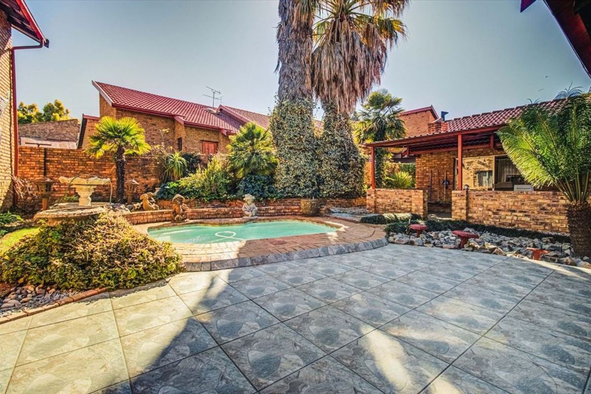 A private outdoor pool area featuring brick paving, a covered patio space, and established garden landscaping with brick boundary walls.