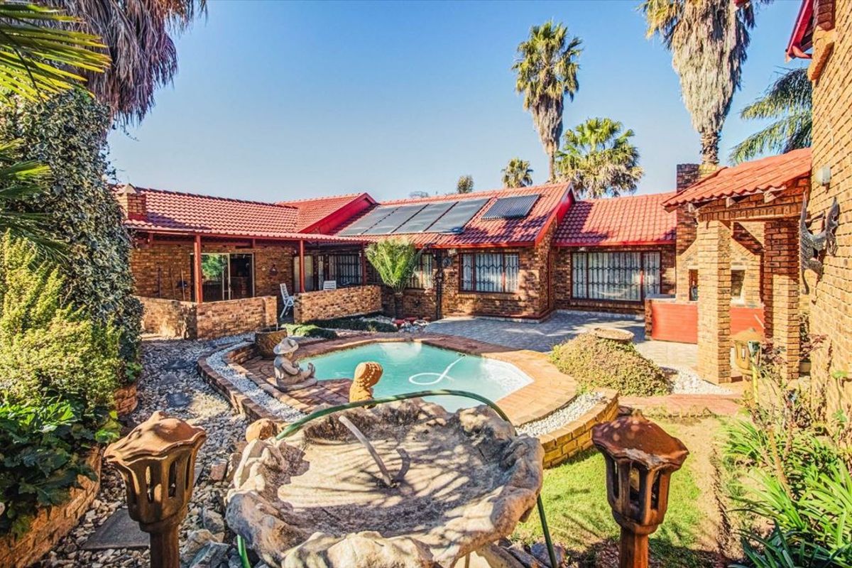 A rear exterior view featuring a swimming pool, brick-paved courtyard, covered patio area, and a house with a tiled roof and solar panels.