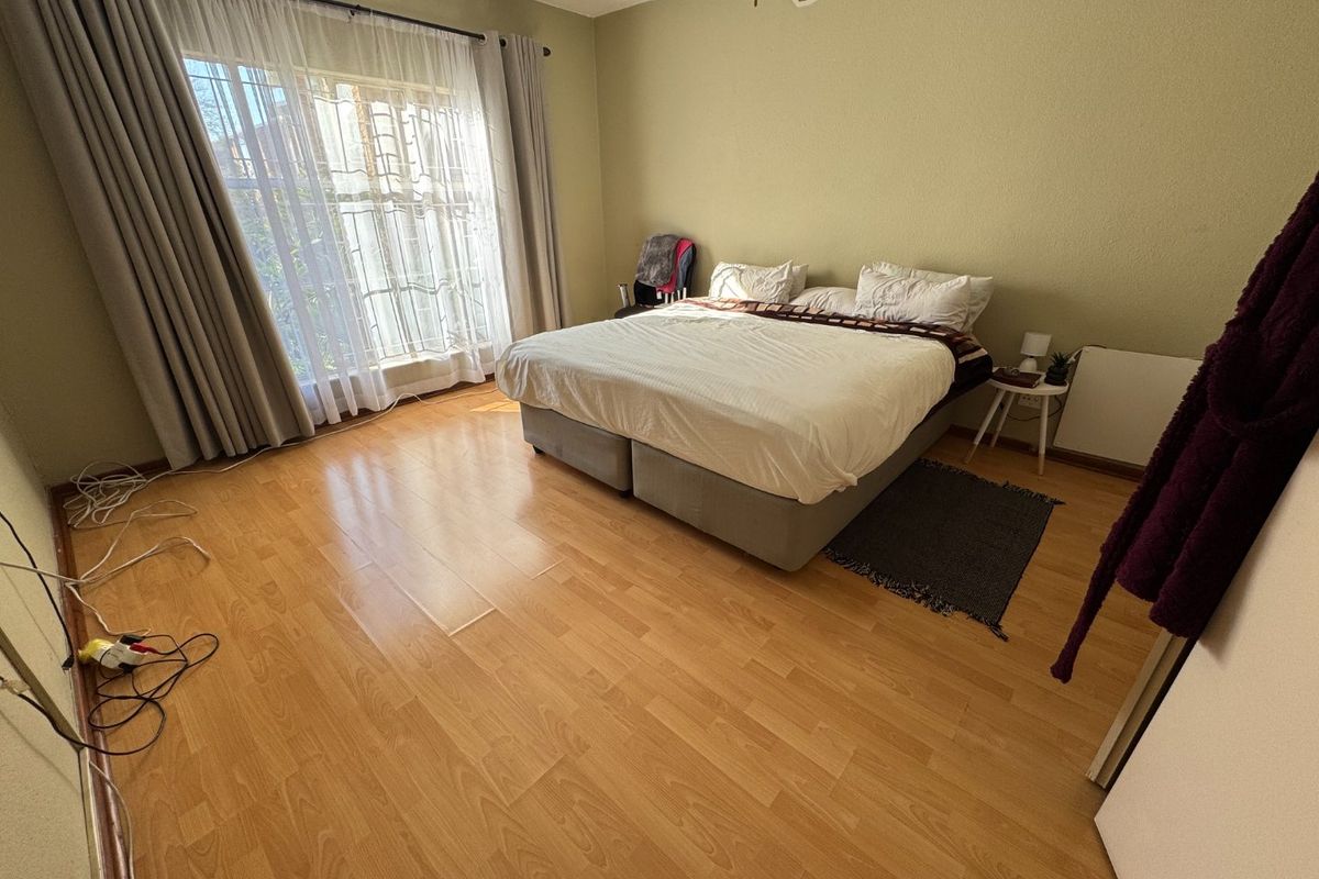 A spacious bedroom featuring light-toned laminate flooring, a ceiling fan, and large windows with installed curtain tracks.