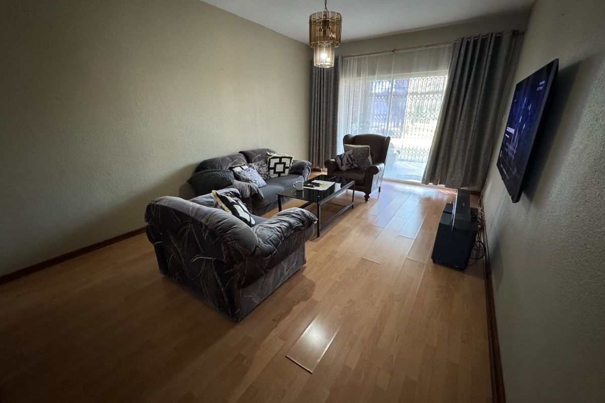 A living room featuring laminate flooring, a pendant light fixture, and a sliding glass door with an integrated security gate leading to the exterior.