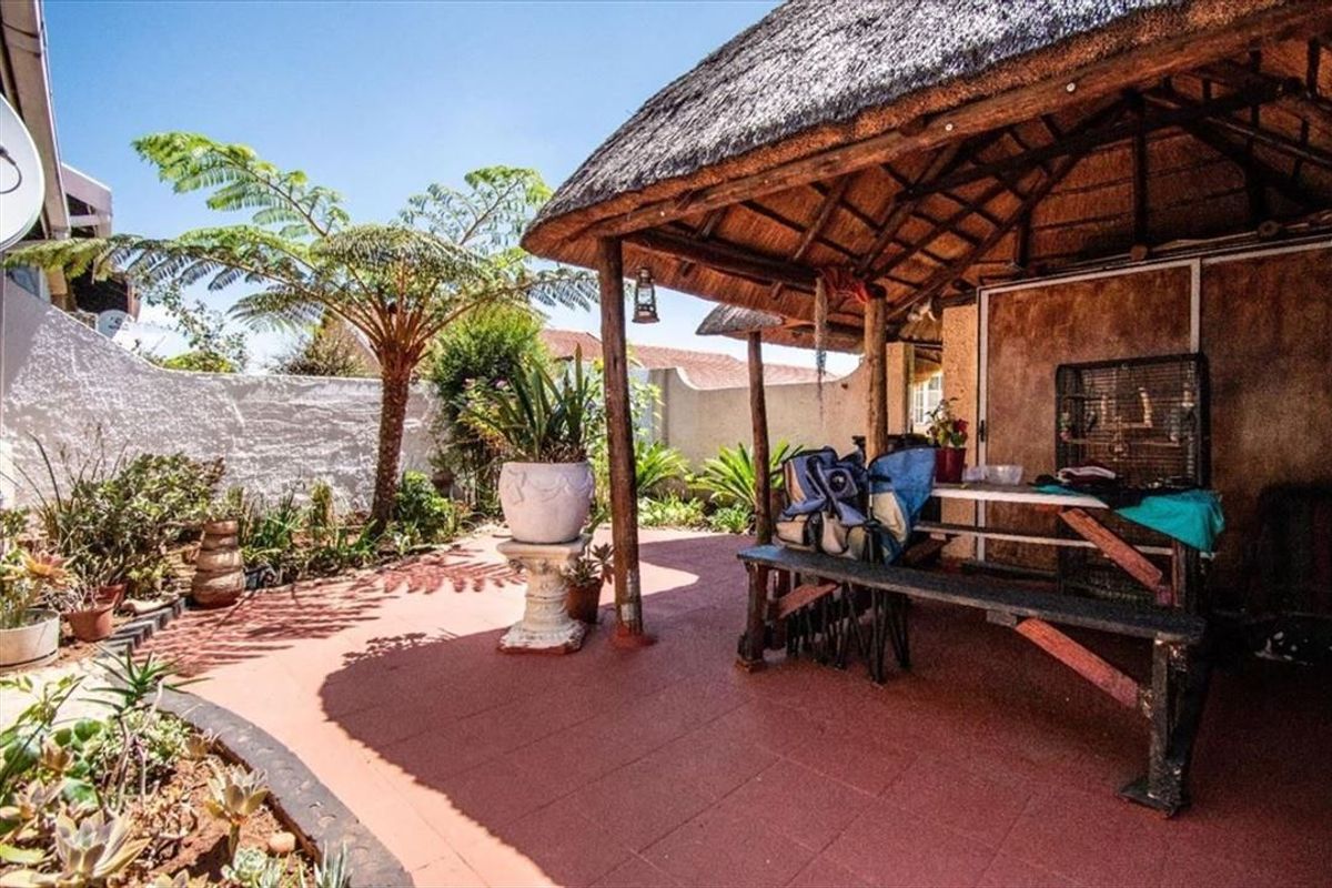 Covered outdoor patio area featuring a traditional thatched roof, timber support structure, and tiled flooring, set within a private garden space.