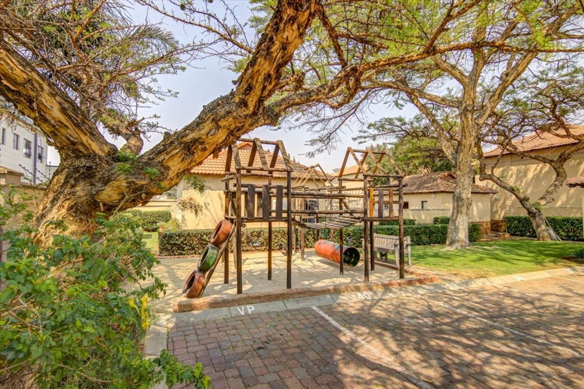 A communal garden area featuring mature trees, landscaped hedges, and brick-paved parking spaces within the townhouse complex.