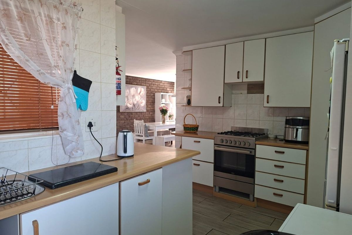 A functional kitchen featuring white cabinetry, laminate countertops, a gas stove with oven, and tiled backsplash, opening into an adjacent dining area.