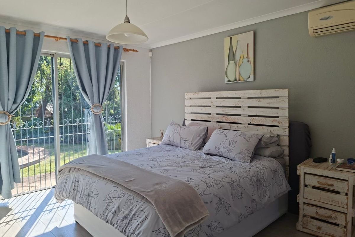 A bright bedroom featuring laminate flooring, a split-system air conditioner, and a sliding glass door with security gate providing access to the garden.