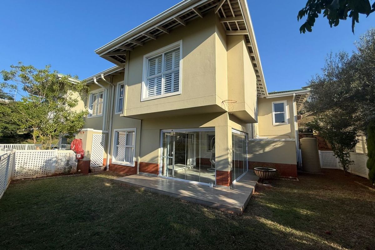 Rear view of the townhouse featuring a private garden, an enclosed tiled patio with sliding glass doors, and well-maintained exterior finishes.