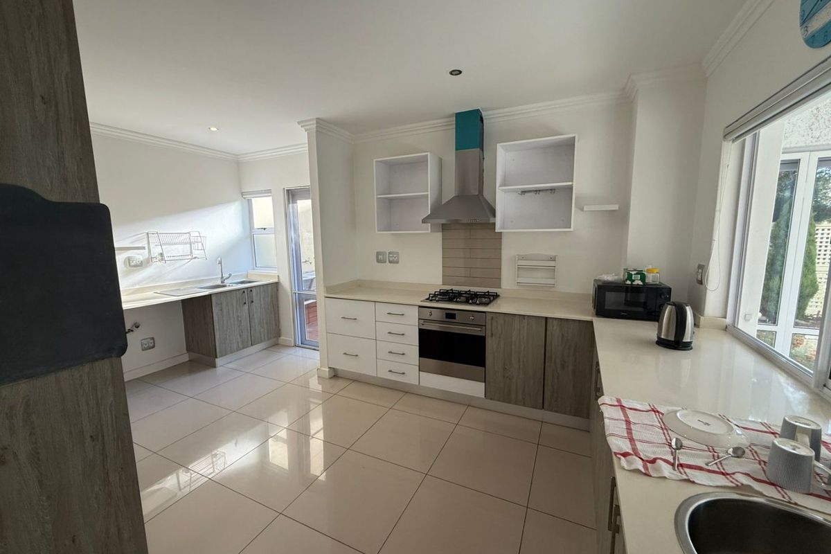 Modern kitchen featuring two-tone cabinetry, stone countertops, gas hob, built-in oven, extractor fan, and tiled flooring with ample natural light.