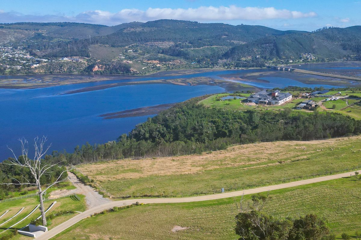 An expansive aerial view of a large residential plot featuring open grassy fields, gravel access roads, and scenic views of the surrounding estuary and hills.