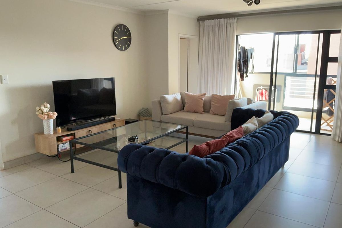 A well-lit living room featuring neutral tiled flooring and large sliding glass doors that provide access to an adjoining balcony.