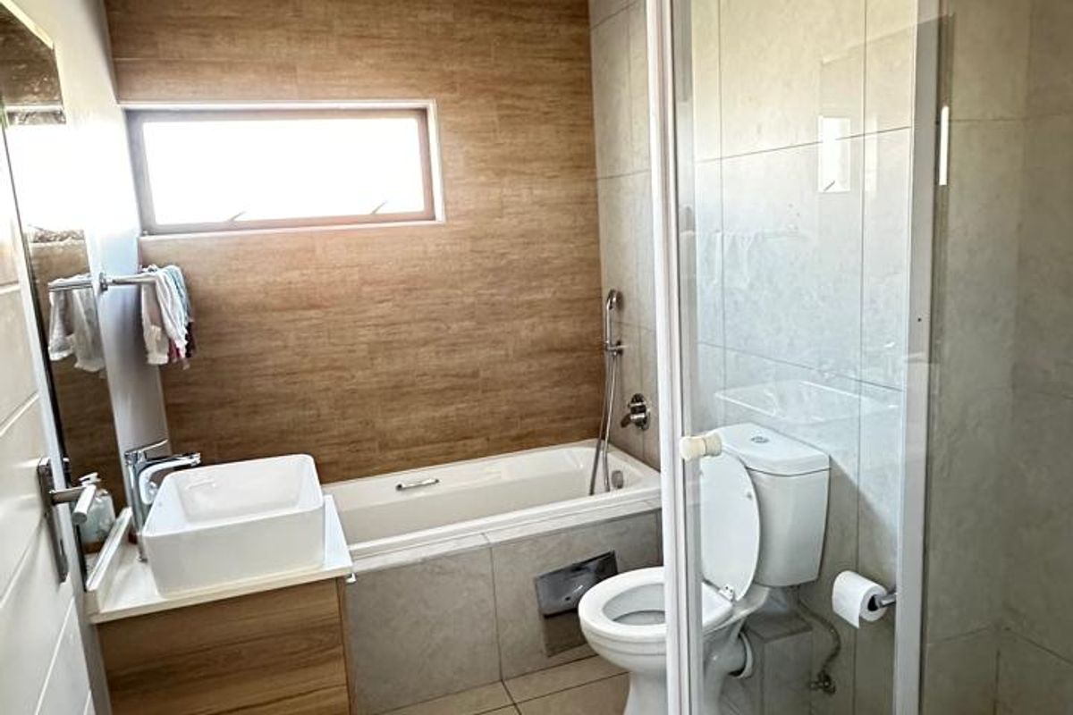 Modern bathroom featuring a glass-enclosed shower, a separate bathtub, a vessel sink vanity, and neutral tiled finishes.