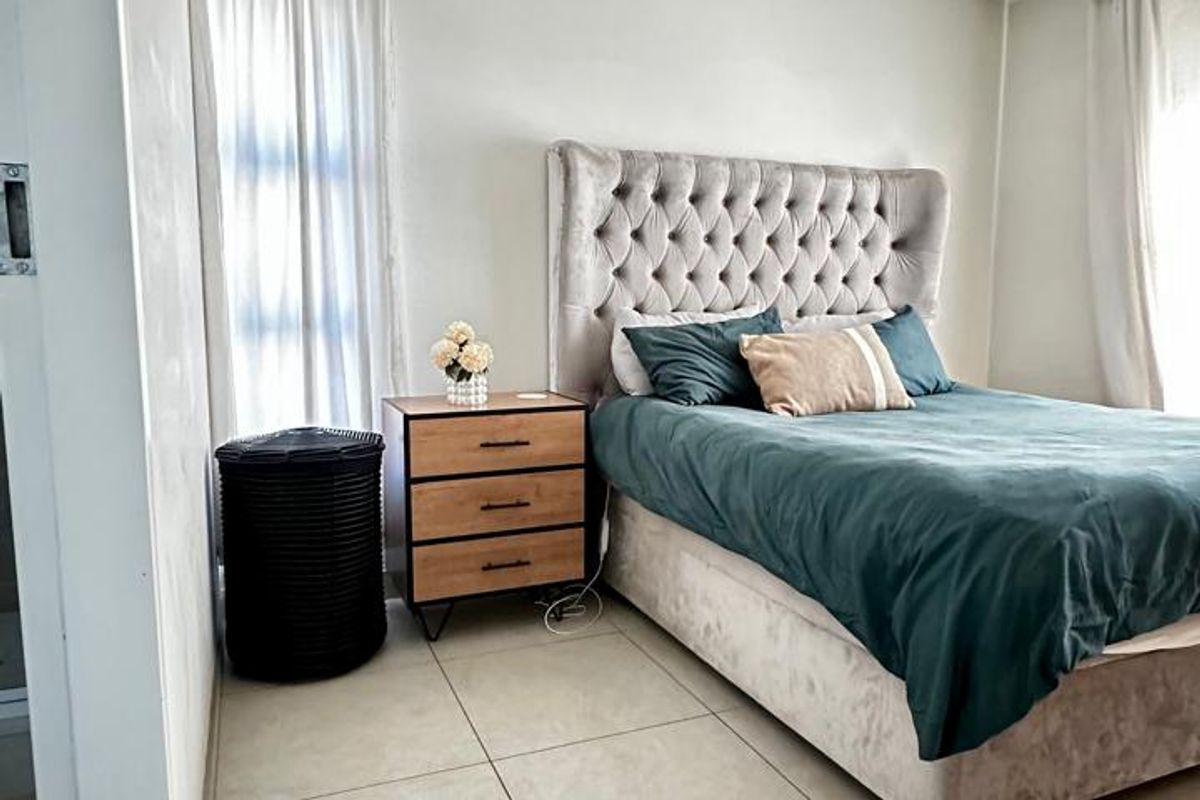 A well-lit bedroom featuring neutral tiled flooring and a clean, modern aesthetic with ample natural light from the windows.