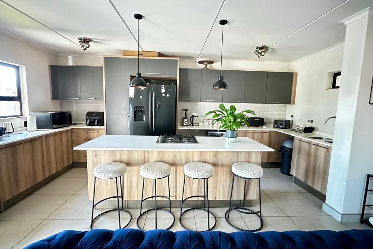 Modern kitchen featuring a central island with a gas cooktop, stone countertops, two-tone cabinetry, and contemporary pendant lighting.