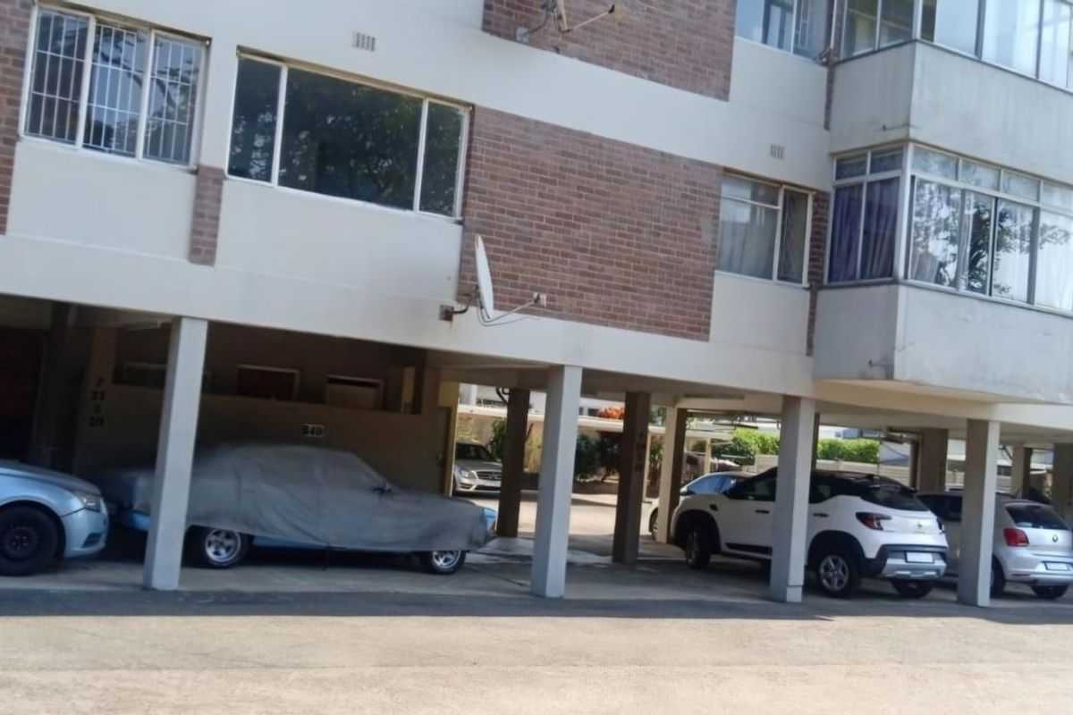 Exterior view of an apartment building featuring a ground-level covered parking area with concrete pillars and brick facade detailing.